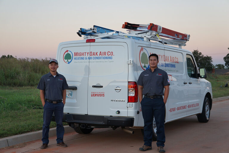 Two HVAC technicians standing next to a Mighty Oak Air Co. van, providing heating and air services.