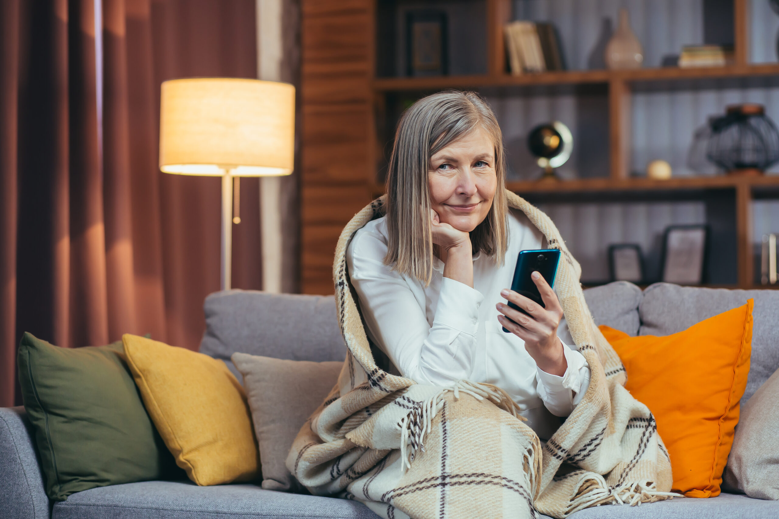 Older woman rests in the evening, talks on video call, uses phone and communication app